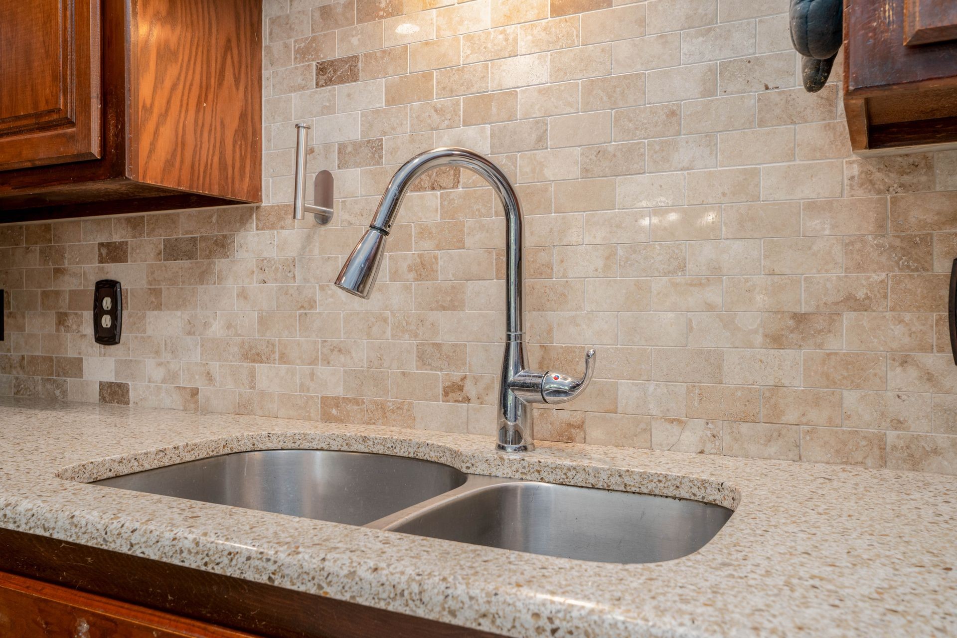 Modern kitchen sink with stainless steel faucet and granite countertop against a beige tiled backsplash.